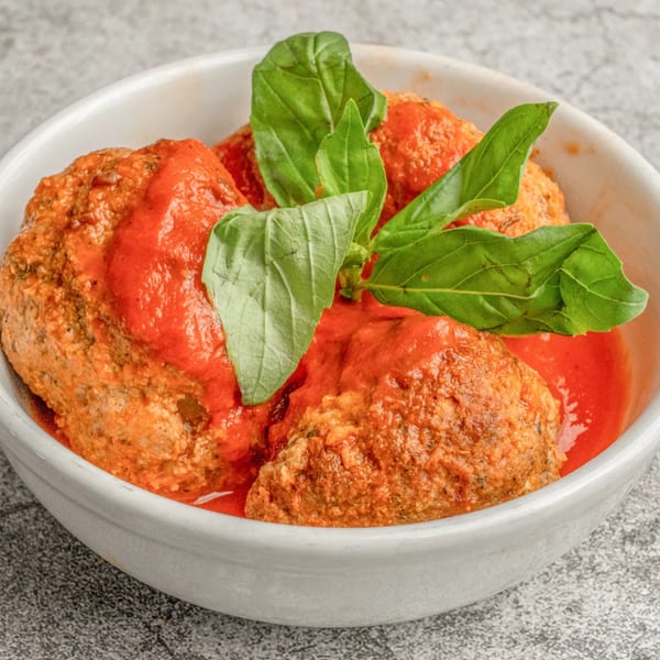 Angelo's Pizzeria's meatballs in red sauce, garnished with fresh basil leaves in a white bowl.