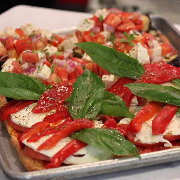 Close-up of Angelo's Pizzeria's bruschetta with tomatoes, mozzarella, basil, and red peppers.