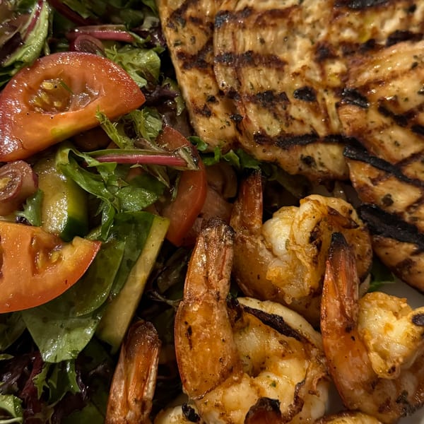Grilled chicken and shrimp with a fresh garden salad, featuring tomatoes and mixed greens.