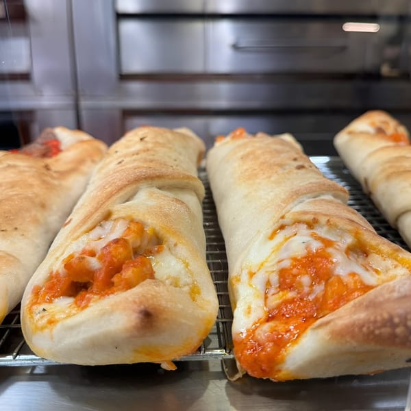 Freshly baked Angelo's Pizzeria calzones with melted cheese and tomato sauce on a cooling rack.